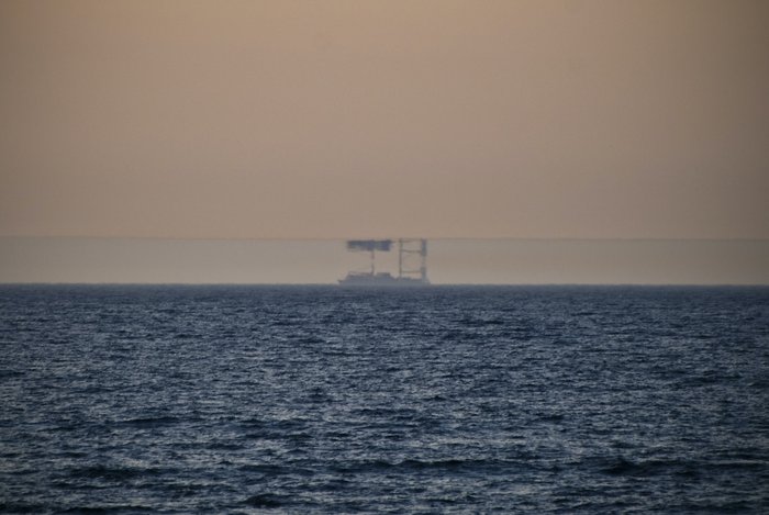 Das Foto zeigt ein Meer in der Abenddämmerung. Am Horizont ist ein Schiff zu erkennen, dass durch eine Luftspiegelung noch einmal auf dem Kopf stehend über dem eigentlichen Schiff zu sehen ist.