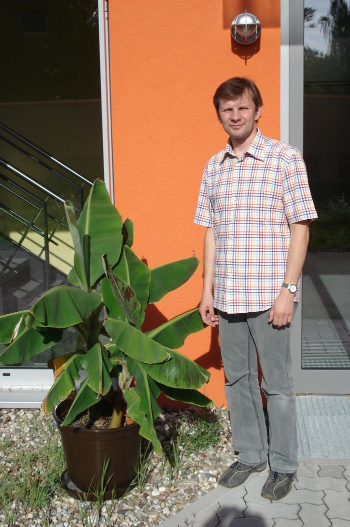 Ein Bild des Forschers vor einer Tür im Freien, stehend neben einer Pflanze.