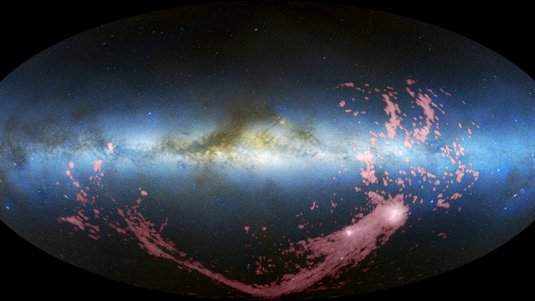 Waagerecht durch das Bild zieht sich die Milchstraße, rechts darunter zwei helle ausgedehnte Objekte, von denen ein langes Band nach links ausgeht.