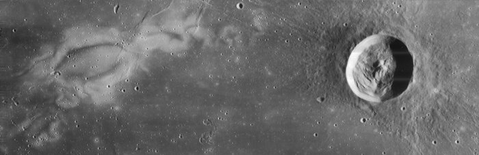 Schwarz-weiß Bild der Mondoberfläche, rechts ist ein kreisrunder Krater zu sehen, links ein weißer, unregelmäßiger Fleck, der noch länger ist als der Krater.