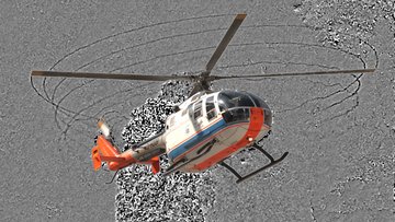Hubschrauber vor Felshintergrund, Wirbel an den Blattspitzen als dunkle Linien sichtbar