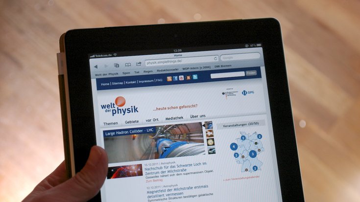 Eine Hand hält einen Tablet-PC, auf dem die Website www.weltderphysik.de zu sehen ist.