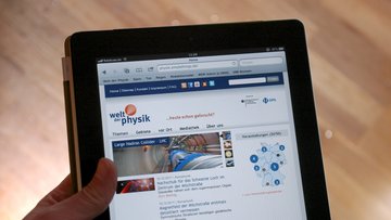 Eine Hand hält einen Tablet-PC, auf dem die Website www.weltderphysik.de zu sehen ist.