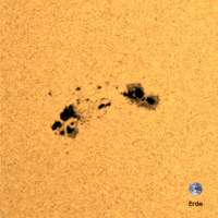 In der Nahaufnahme ist ein Sonnenfleck zu sehen, also eine dunklere Region auf der Sonnenoberfläche, die einige tausend Grad Celsius kühler ist als die umgebende Oberfläche. Rechts unten im Bild befindet sich die Erde maßstabsgetreu zum Größenvergleich. 