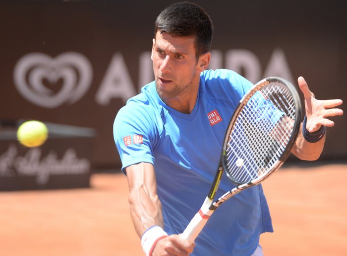 Der Spieler Novak Đoković mitten in der Bewegung, er hält einen Tennisschläger vor ihm ist der Ball zu sehen.