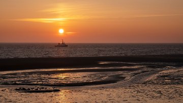 Meeresufer bei Ebbe im Sonnenuntergang mit Schiff im Hintergrund