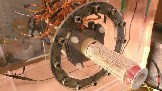 Das Bild zeigt den experimentellen Aufbau aus vielen Kabeln, einem Metallring und einer zylindrischen Röhre.