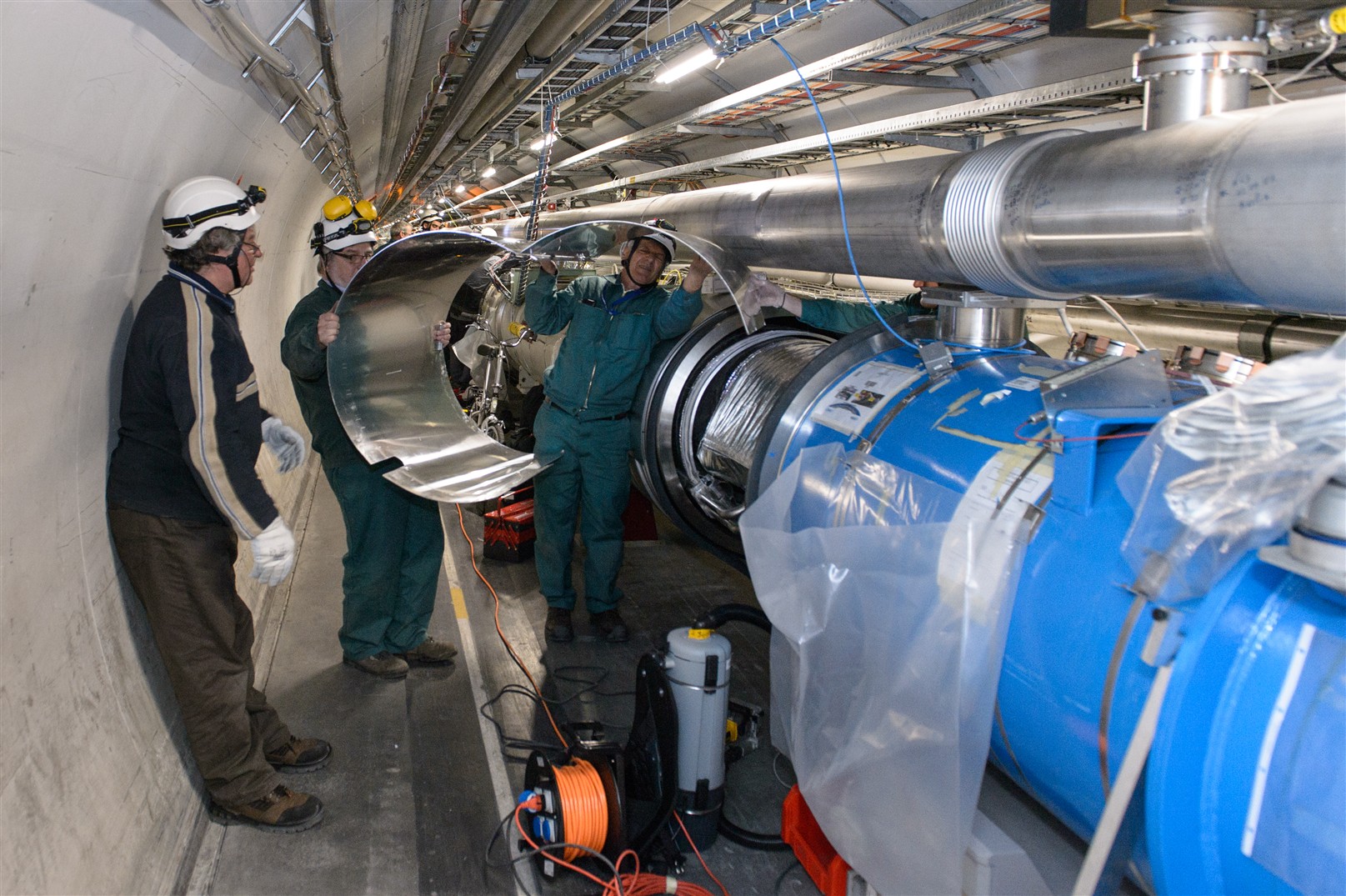 Männer im LHC-Tunnel, die eine Verbindungstelle zwischen Magneten öffnen.
