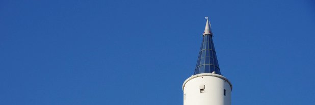 Das ZARM in Bremen, Foto: Jens Kube Vor einem wolkenlosen Himmel ragt die verglaste Spitze eines schlichten, glatten Turms auf.