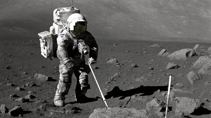 Schwarz-weiß-Foto eines Astronauten auf dem Mond, der einen Stab in der Hand hält und einen großen Rucksack auf dem Rücken trägt
