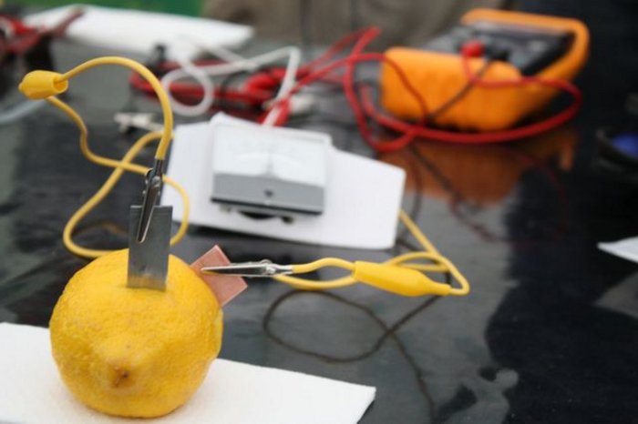 Experimente für Schüler Zitrone mit Klemmen und Kabeln, die zu einem Strommessgerät führen.