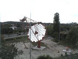 Ein CTA-Teleskop steht auf einem kleinen Platz, im Hintergrund sind Wohnhäuser zu erkennen.