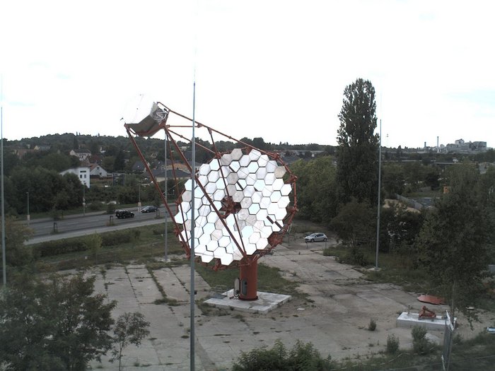 Prototyp eines CTA-Teleskops Ein CTA-Teleskop steht auf einem kleinen Platz, im Hintergrund sind Wohnhäuser zu erkennen.