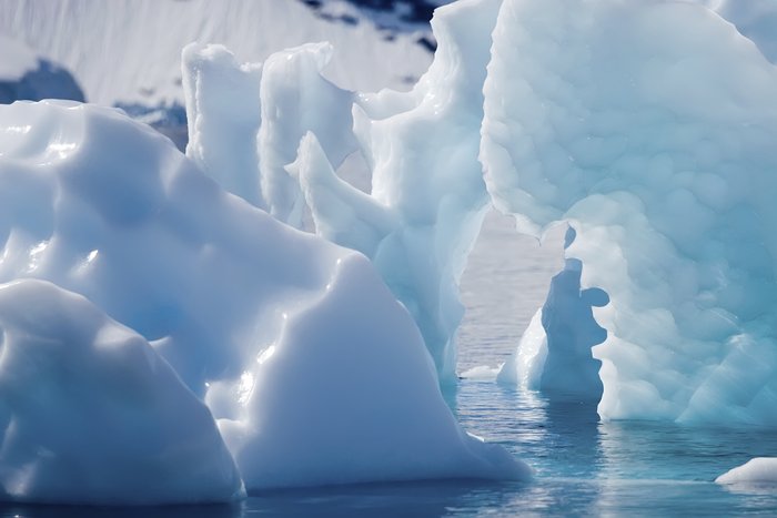 Ein Eisberg mit einer deutlichen Blaufärbung und verschiedenen Einschlüssen von Verunreinigungen. Er hat fast die Farbe des Himmels.