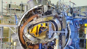 Die Aufnahme zeigt einen Ingenieur im Inneren der sich im Aufbau befindlichen Experimentieranlage Wendelstein 7-X. Der Ingenieur befindet sich im inneren Torus, in dem inzwischen das Verhalten von Wasserstoffplasma untersucht wird. 