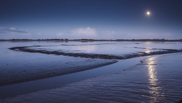 Wattenmeer in der Dämmerung mit einem am Himmel stehenden Mond