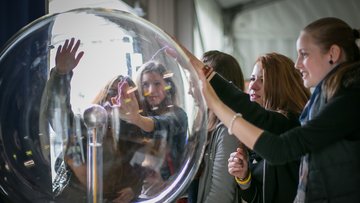 Das Bild zeigt Besucherinnen der Highlights der Physik, die mit einer Plasmakugel experimentieren.