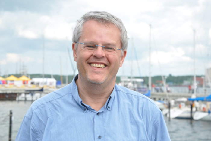 Stefan Jordan Lachender, grauhaariger Herr mit randloser Brille und einem schlichten, leicht zerknitterten Hemd.