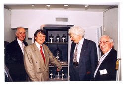 Klaus von Klitzing und weitere Herren in Anzügen vor dem offenen Safe mit dem Ur-Kilogramm, dass sich unter einer von mehreren Glasglocken befindet.