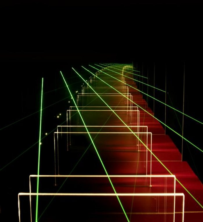 Optischer Resonator System von Spiegelpaaren, die in einer langen Reihe jeweils parallel zueinander stehen. Darüber sind grüne Lichtstrahlen zu sehen.