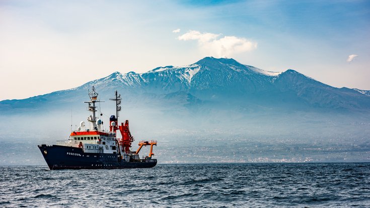 Das Bild zeigt ein Schiff, das sich auf dem Meer vor einem Berg befindet.