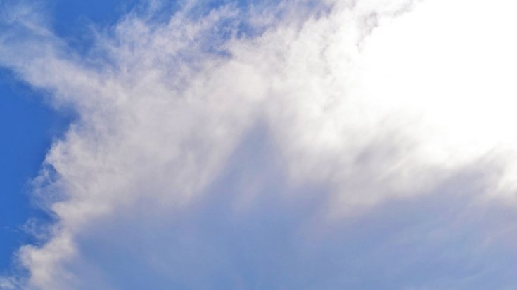 Langgezogene, zur Mitte hin dunkelgrau werdende Wolke an einem blauen Himmel