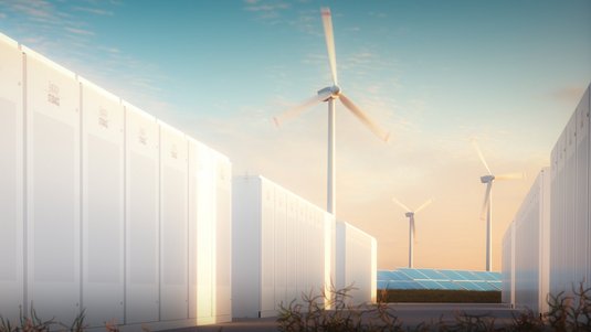 Die Illustration zeigt eine Landschaft mit Windrädern und Solarzellen, im Vordergrund sind Gebäude zu erkennen, in denen sich Energiespeicher befinden.