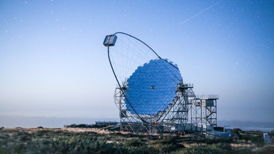 Großes Teleskop auf einer Wiese. Im Hintergrund ist der Himmel ohne Wolken zu sehen.