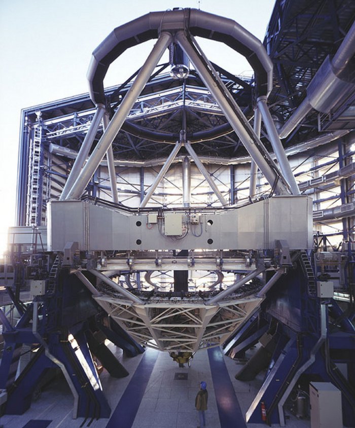 Teleskop des VLT von innen Riesiges Metallgerüst, unterhalb ein Mann, der winzig dagegen wirkt. Oberhalb eine geöffnete Hallendecke, durch die man den Abendhimmel sieht.
