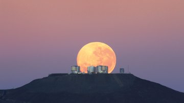 Mond am Horizont hinter Teleskopen auf einer Bergkuppe