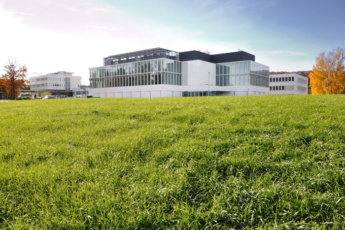 Bungalowartiges Gebäude aus Glas, Beton und Stahl auf einer grünen Wiese.