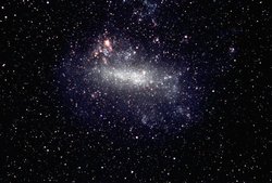 Ein nebelartiger Fleck auf schwarzem Hintergrund. Einzelne Sterne, aus denen der nebelartige Fleck besteht, sind zu erkennen.