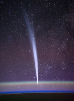 Komet mit langem dünnen Schweif, unten der Erdrand mit atmosphärischem Schleier