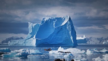 Ein großer Eisberg ragt aus dem Wasser, davor ein Boot mit Menschen.