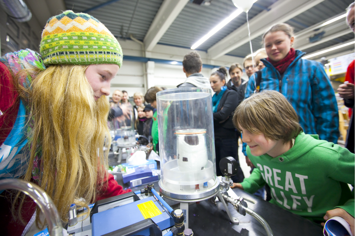 Besucher bei der Nacht des Wissens am DESY 2011 Ein Mädchen und ein Junge schauen in eine Vakuumglocke, in der sich gerade ein Schokokuss unter Einfluss des Vakuums aufbläht. Im Hintergrund sind weitere Besucher zu sehen.
