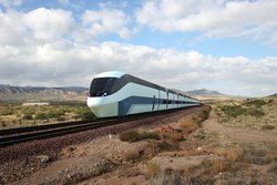 Ein futuristischer Zug saust durch eine karge Landschaft. Er hat getönte Fenster und sportliche Streifen an der Seite.