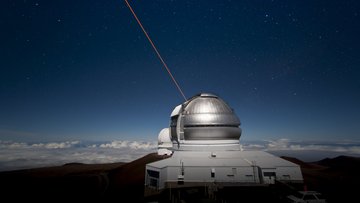 Großes rundes Teleskop steht auf einer Erhöhung in der Landschaft.