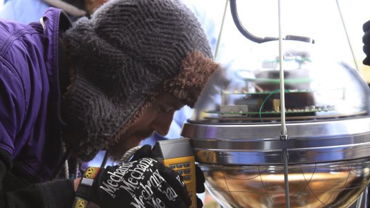 Forscher mit Fellmütze vor einem Sensor von IceCube.