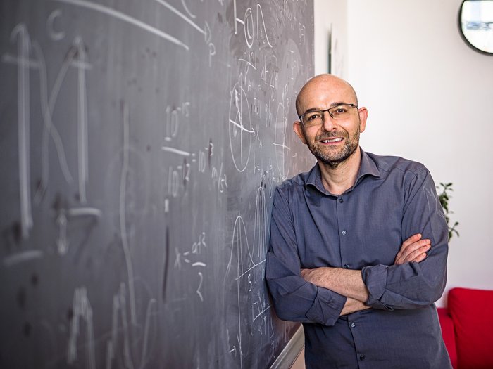 Caslav Brukner Das Bild zeigt den Forscher, der an eine, mit mathermatichen Formerln beschriebene Tafel lehnt.