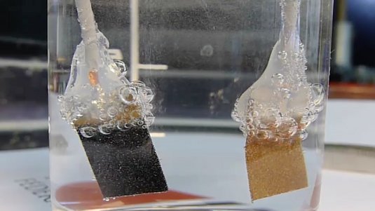 In einer wassergefüllten Glas entstehen Bläschen aus Sauerstoff an der linken und Wasserstoff an der rechten Katalyse-Elektrode