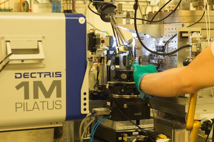 Mit Röntgenstrahlen werden Nanodrähte untersucht Eine behandschuhte Hand setzt einen Chip, auf dem sich die Nanodrähte befinden, in einen Versuchsaufbau ein.