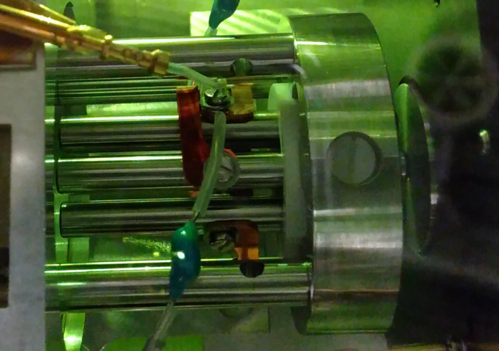 Interaktionsregion Das Bild zeigt den experimentellen Aufbau: Mehrere Röhren verlaufen zwischen zwei Metallscheiben. Von oberhalb kommen zwei Schläuche zum Experiment.