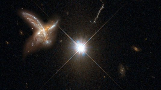 Das Bild zeigt die künstlerische Darstellung eines Quasars, der hell und punktförmig leuchtet. Links davon ist eine benachbarte Galaxie abgebildet, sowie andere Sterne im Hintergrund.