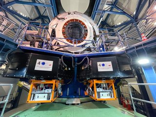 In einer Maschinenhalle befindet sich oben unter dem Dach ein großes Objektiv. Es ist über eine vorgelagerte Tribüne erreichbar. Darunter hängen zwei kubusartige Kammern, in denen Computer stehen.