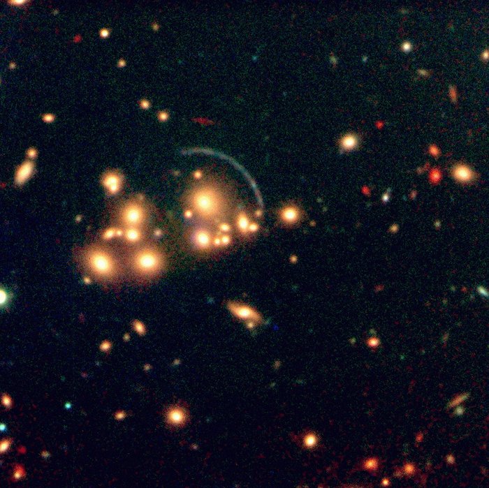 Der Galaxienhaufen Cl2244-02 Himmelsaufnahme mit einem Haufen gelber Objekte; etwas daneben ein dünner blauer Kreisbogen von einem Viertel-Kreis; die Mitte des Kreises liegt im Zentrum im Haufen der gelben Objekte.