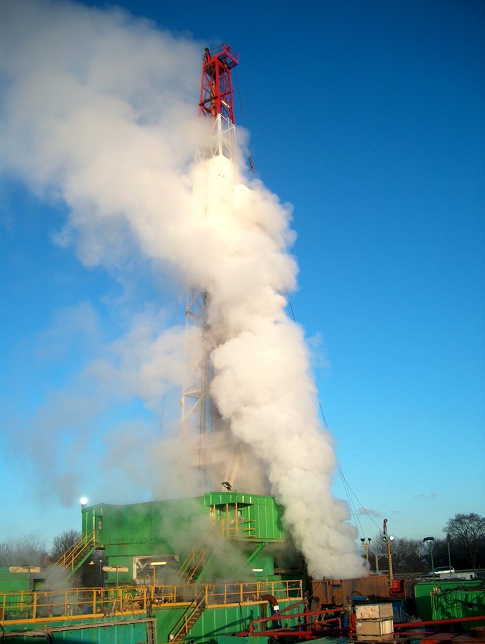 Anlage mit Bohrturm, aus einer Öffnung steigt eine große Dampfsäule.