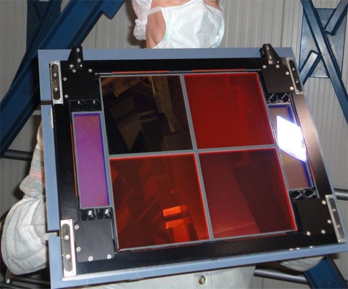 Filterglas Eine Person mit Mund- und Kopfschutz hält einen quadratischen Rahmen, in dem sich vier quadratische Filterglasscheiben wie Quadranten befinden.