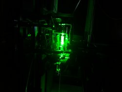 Grünes Laserlicht leuchtet aus einer Apparatur heraus, der Hintergrund ist dunkel.