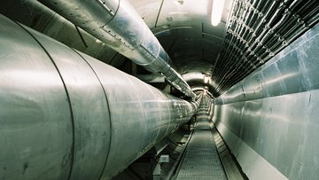 Das Bild zeigt einen Fernwärmetunnel durch den zwei Rohre zur Dampfleitung verlaufen, am rechten Rand verlaufen mehrere Stromkabel.