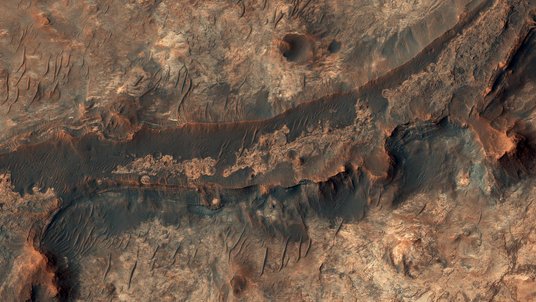 Luftaufnahme einer felsigen Landschaft auf dem Mars, auf dem eine geschwungene Vertiefung zu erkennen ist